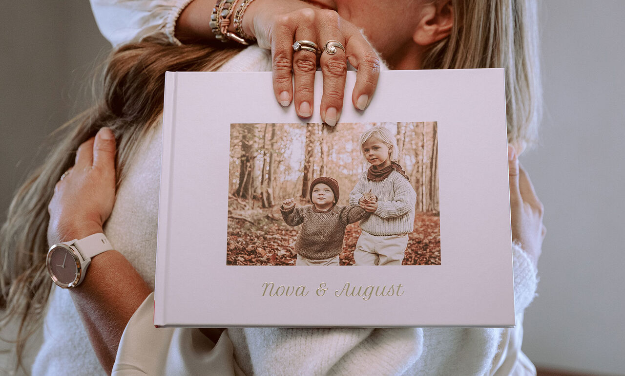 En person håller en fotobok med en bild på två barn i en skog.