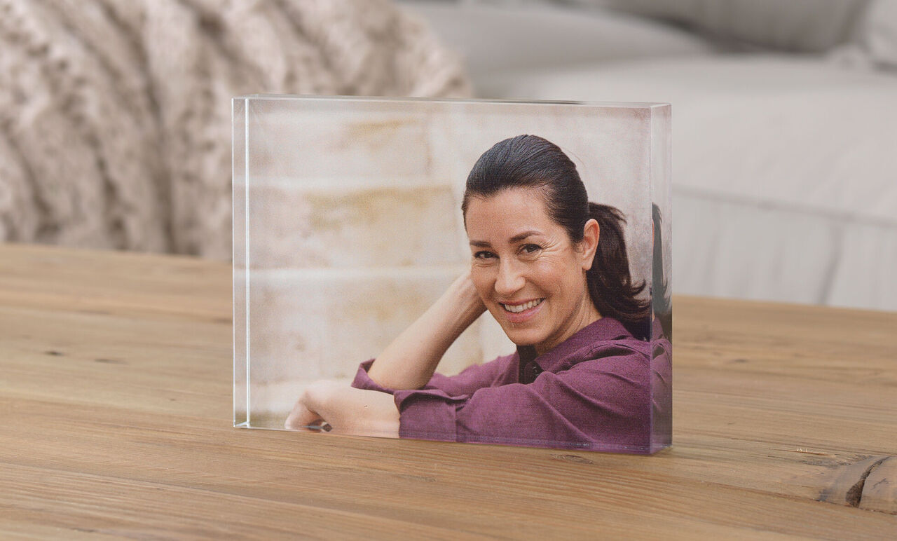 Transparent foto i en block på ett träbord, person sitter avslappnat och ler.
