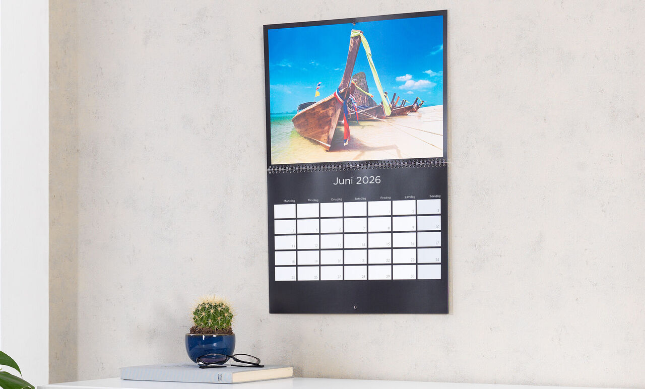 En väggkalender visar en bild av en båt på stranden, med juni 2025 under.