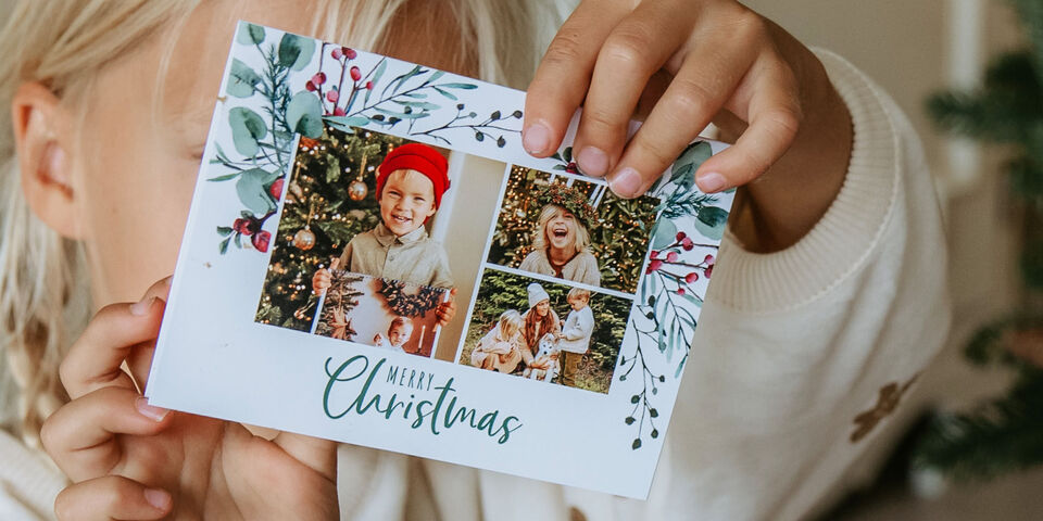 Ett barn håller ett festligt julkort med bilder och en krans.