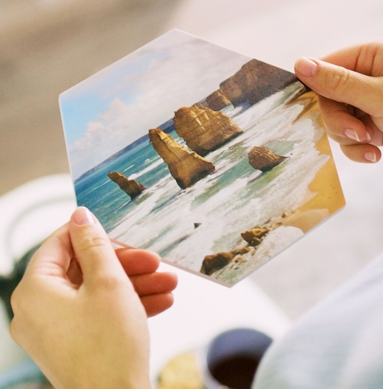 En person håller ett hexagonalt fotokort med de berömda Twelve Apostles vid Australiens kust.
