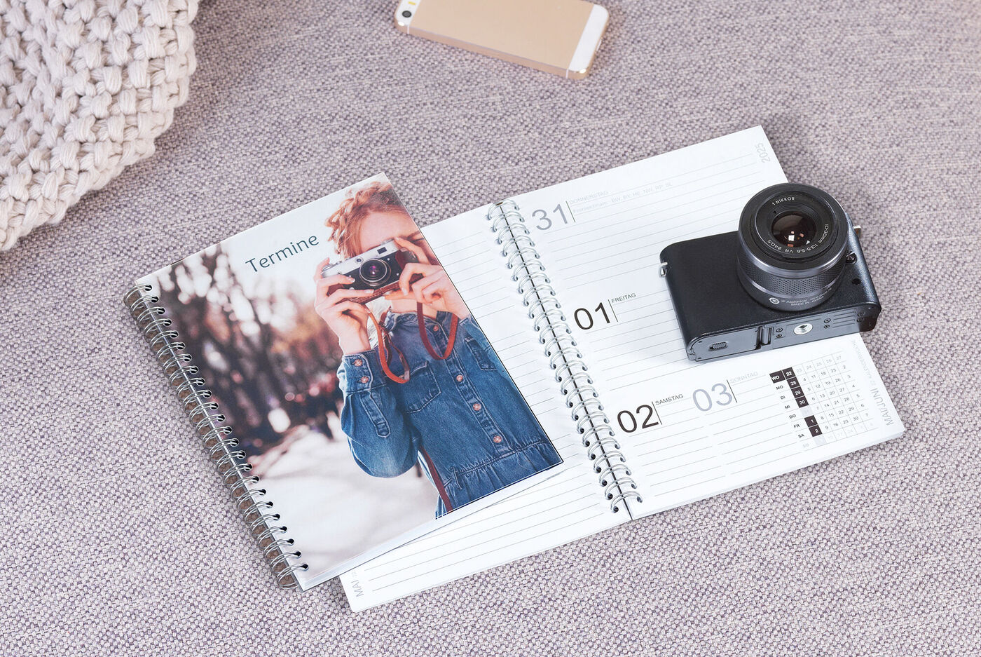 En kalender ligger öppen på ett bord bredvid en kamera och en fotobok.