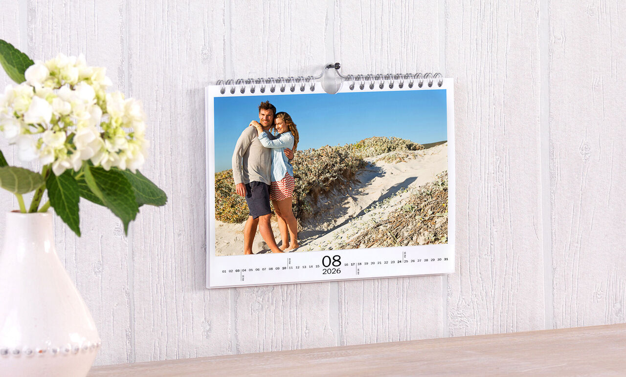 En vacker väggkalender med foto av ett par på stranden. Kalendern visar augusti 2023.