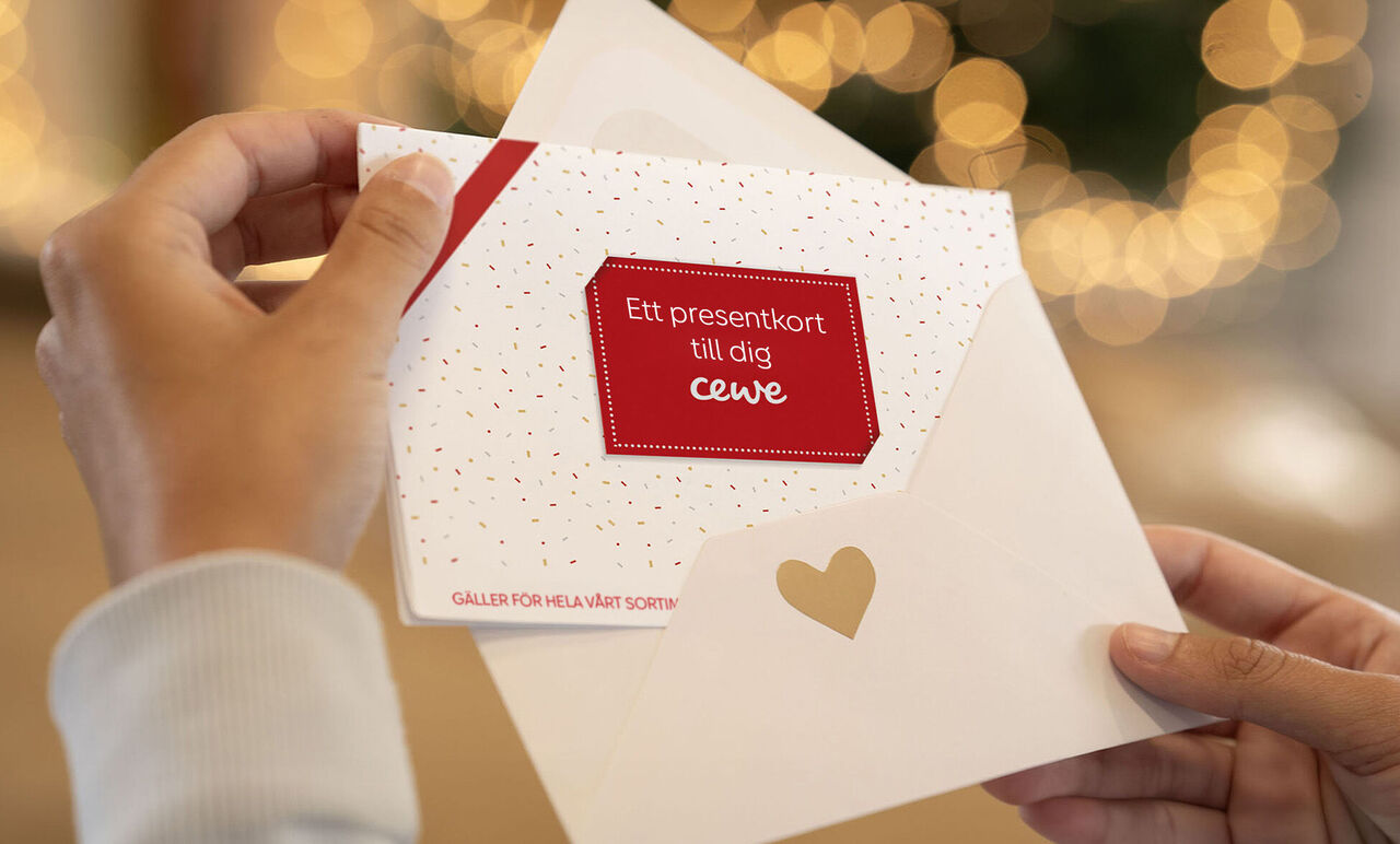 En hand håller en öppen CEWE gratulationskortomslag med ett presentkort.