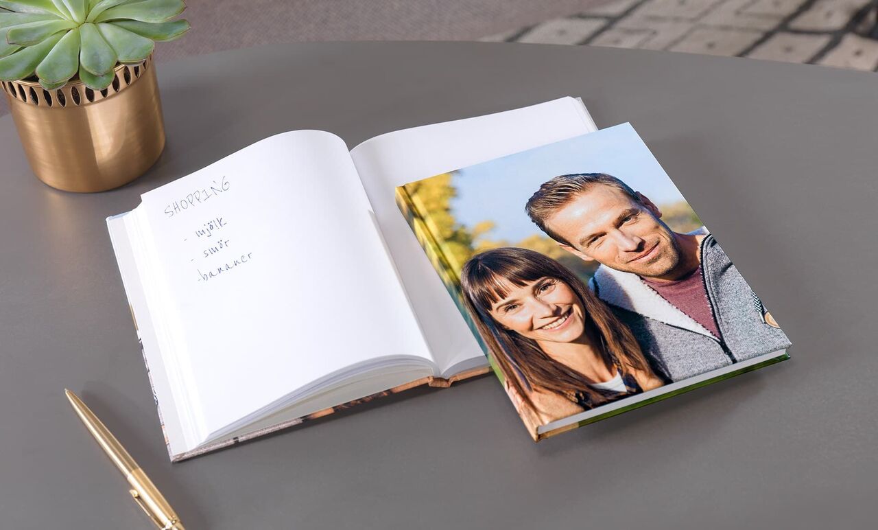 En öppen fotobok med ett fantastiskt omslag och en tom insida. Bredvid ligger en gyllene penna.