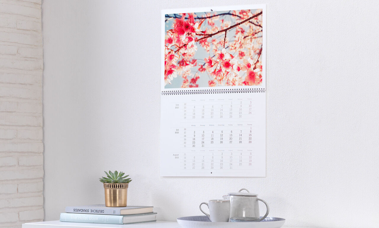En CEWE fotokalender med blommande körsbär och en ljus bakgrund hänger på väggen.