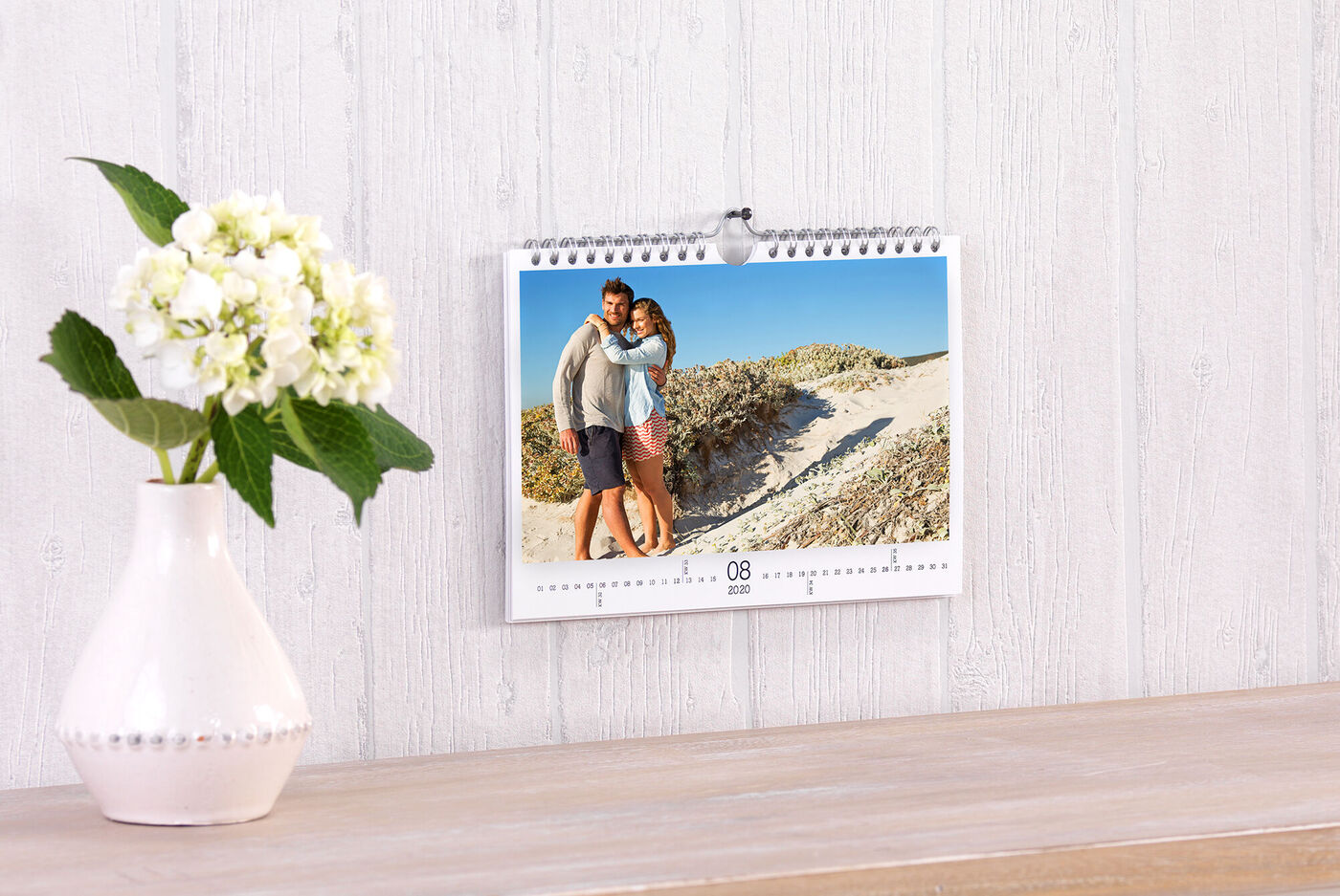En kalender hänger på väggen. På kalendermotivet ser man ett par som kramas, med en sandstrand i bakgrunden.