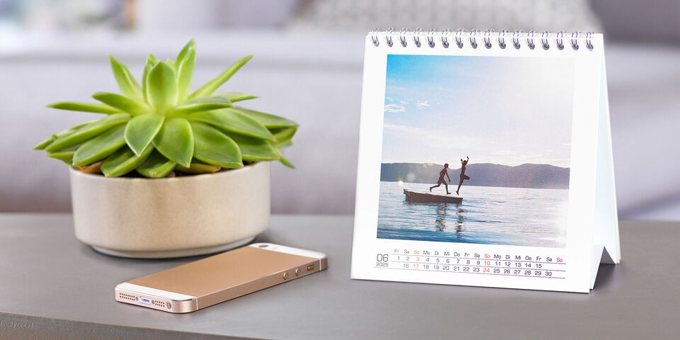 En liten bordskalender med en bild av två personer som står på en båt och njuter av vattensport. I bakgrunden syns mjuka vågor och en vacker landskap.