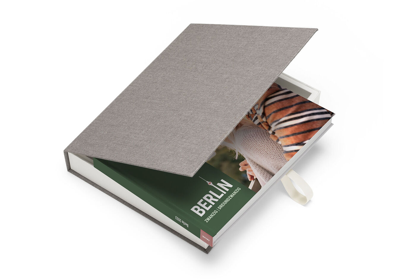 En öppen CEWE FOTOBOK med en bild av Berlin inuti och ett grått tygomslag.