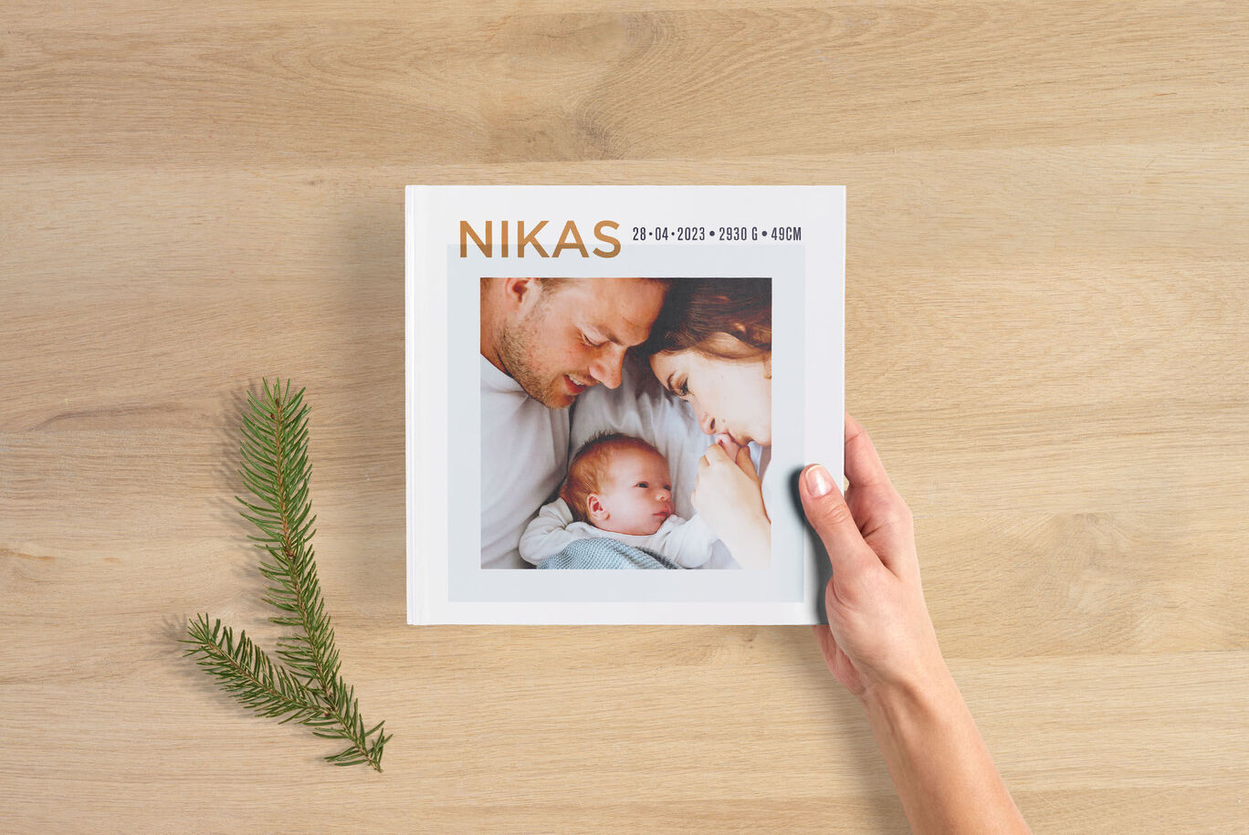 En hand håller en CEWE fotobok med en babybild och en trevlig design.