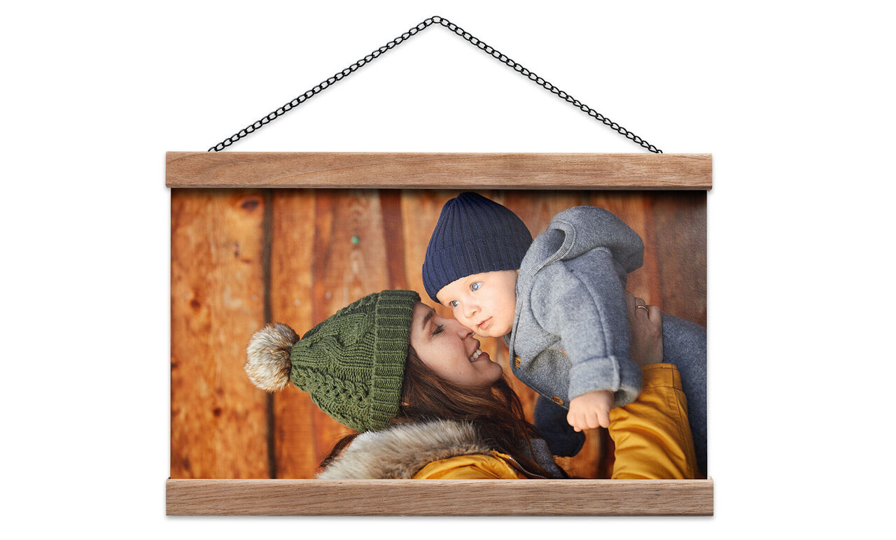 En leende mamma håller sitt baby i varma kläder vid en trävägg.