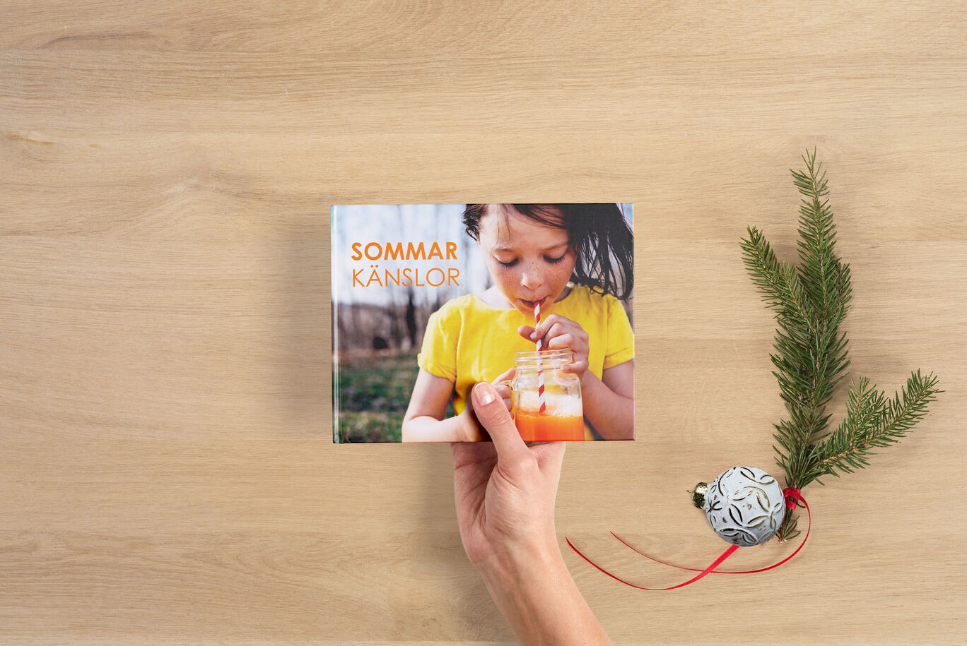 En person håller en CEWE fotobok med titeln "Sommarkänslor".