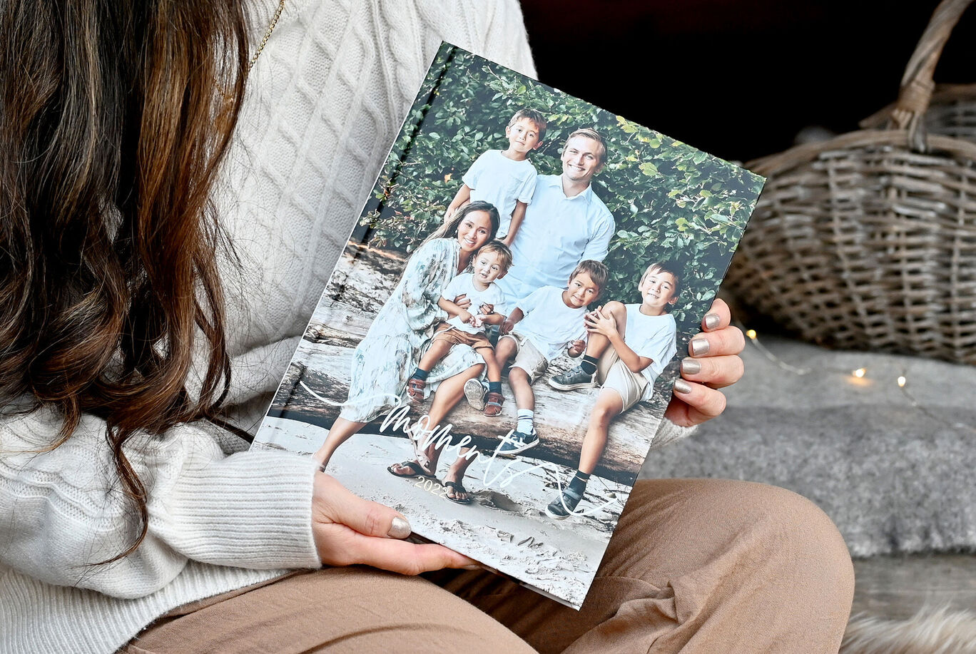 En person håller kärleksfullt ett CEWE Fotoalbum med familjebilder på en plats i naturen.