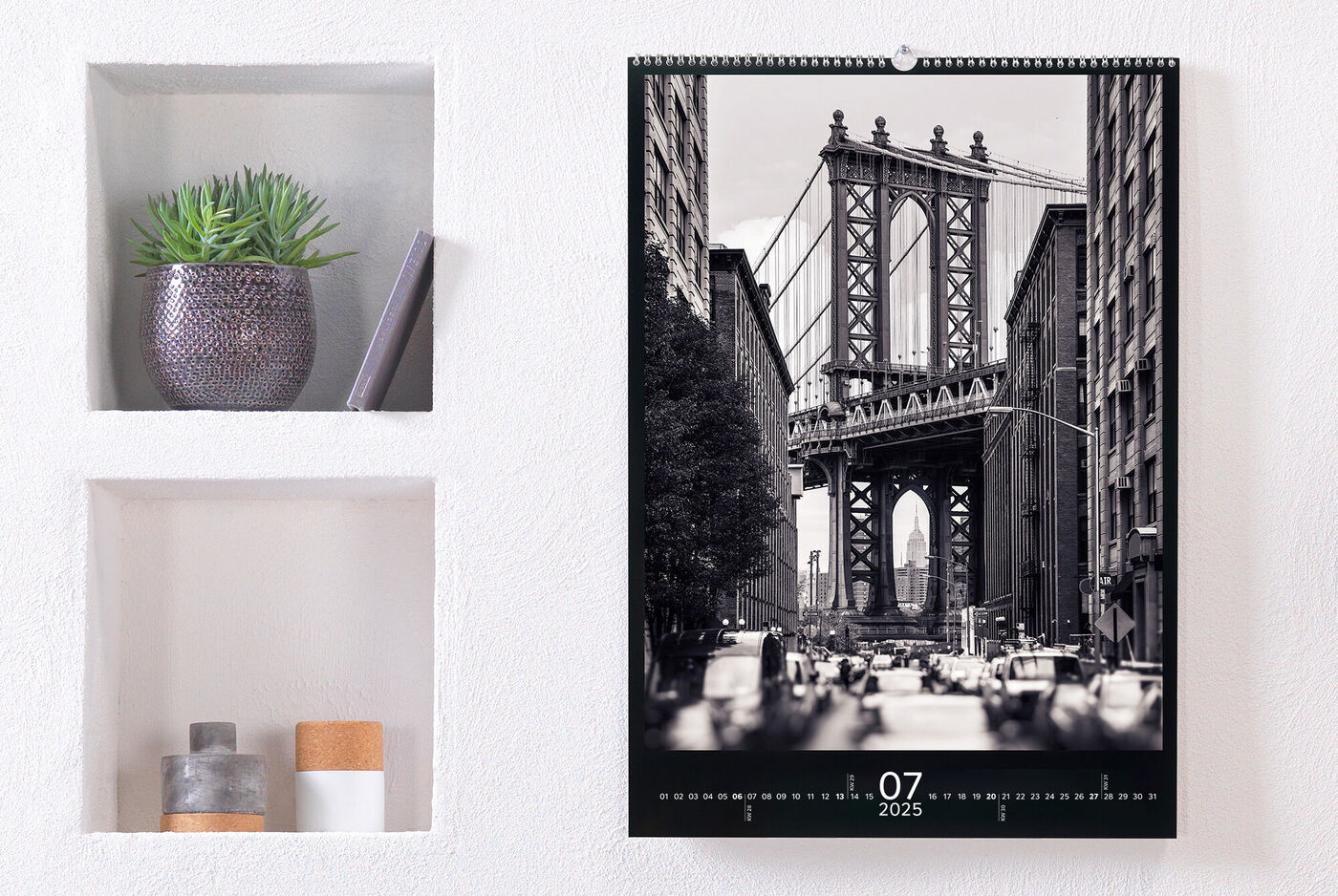 En stilren fotokalender hänger på en vägg. Juli 2025 syns med en bild av Brooklyn Bridge i svartvitt.